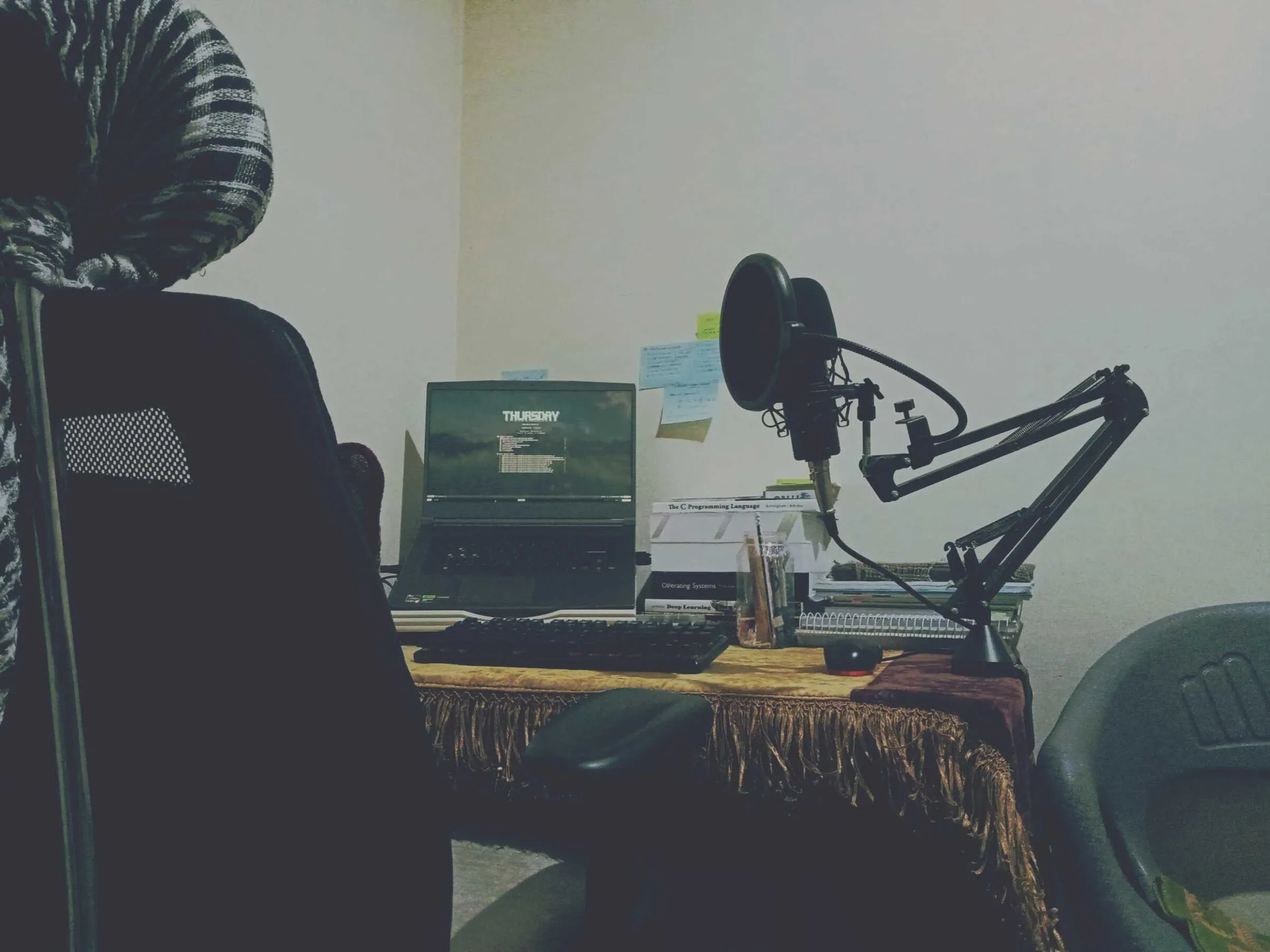 The same desk seen from behind an office chair: laptop, microphone arm and books